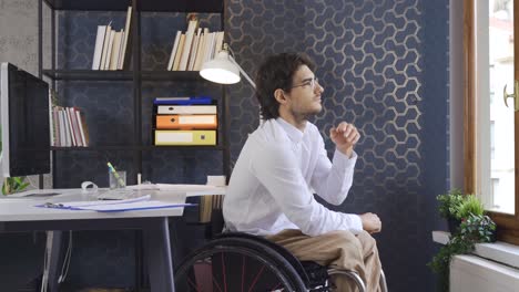 Disabled-man-in-wheelchair-works-in-office-and-is-thoughtful.